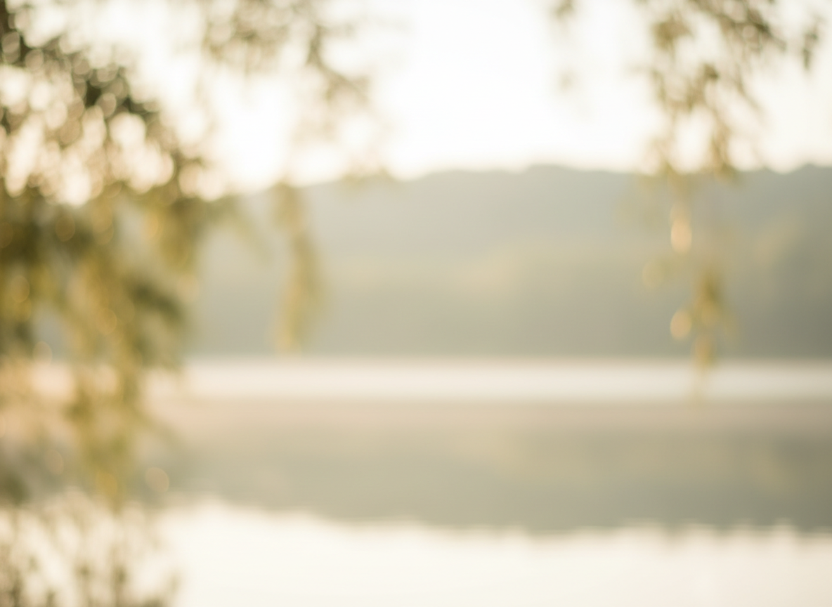 A soft, calming abstract nature photograph in warm muted tones — gentle morning light filtering through out-of-focus soft foliage or a calm still lake at dawn, warm cream and muted sage green palette, serene and grounding, no people, soft natural blur, reassuring atmosphere